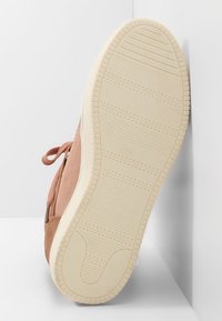 Podešev béžové tenisky s texturovanými vzory pro lepší přilnavost a nápisem značky, tkaničky viditelné na straně, umístěné na bílém rohovém pozadí.