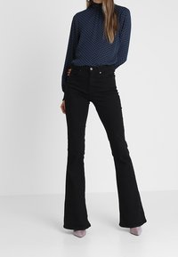 Svarta utsvängda jeans med hög midja, tillverkade av denim. Matchas med en marinblå blus med vita prickar och långa ärmar.