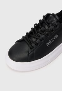 Melna sintētiska sneaker ar noapaļotu purngalu, laces priekšā un balto gumijas zoli. Iespējas iebrauktā zīmola detaļa sānos. Gluda tekstūra.