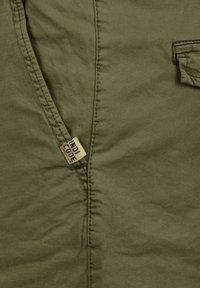 Tela de color verde oliva con una textura suave, que presenta costuras cosidas y una etiqueta que dice "INDI CODE" sujeta al costado.