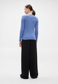 Zils adījuma džemperis ar piegulošu augumu, apaļu apkakli un garām piedurknēm, kombinēts ar vaļīgām melnām plašām biksēm.