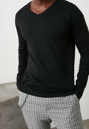 Czarna, długorękawowa koszula z dekoltem w serek, zestawiona z szaro-białymi, kratkowymi spodniami, wykonana z gładkiej tkaniny o dopasowanym kroju.