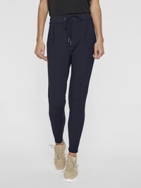 Navy blue jogger pants made of soft fabric, featuring a drawstring waist, two side pockets, and tapered legs, paired with beige sneakers.