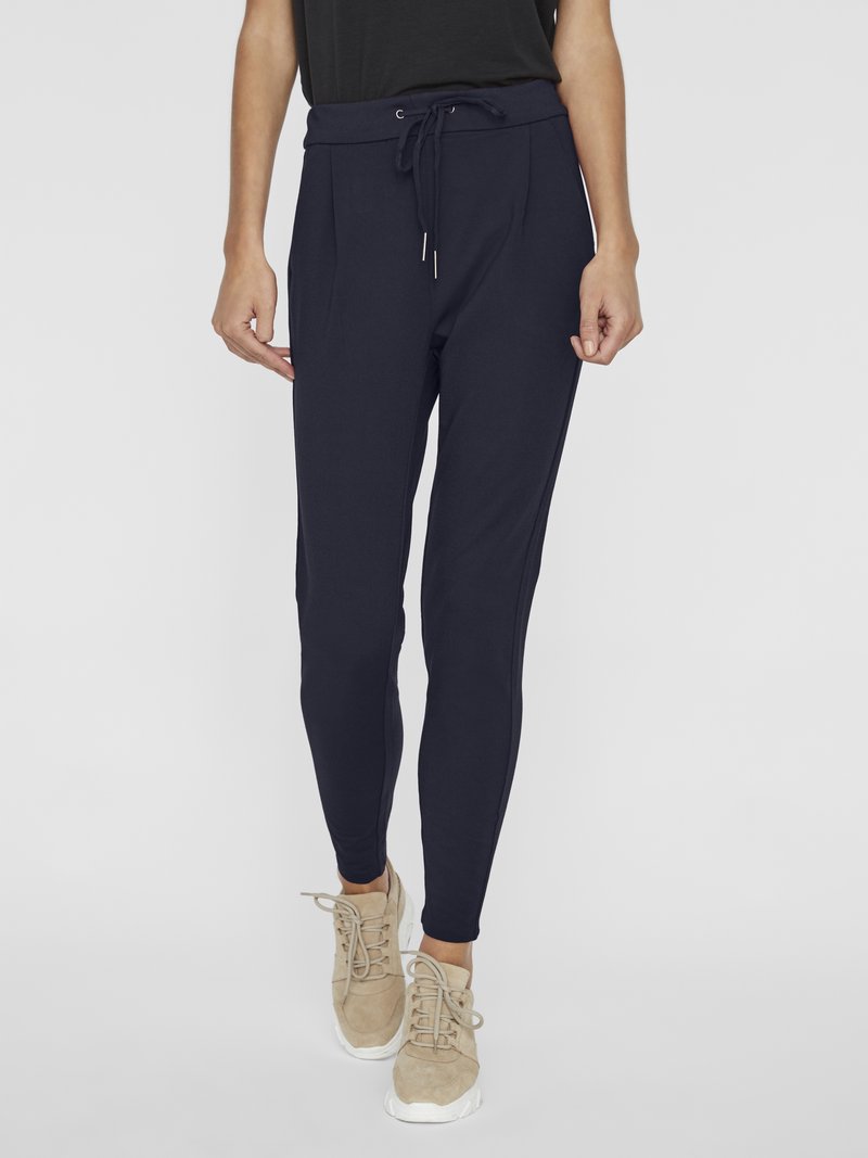 Marinblå joggingbyxor i mjukt tyg, med dragsko i midjan, två sidofickor och avsmalnande ben, i kombination med beige sneakers.