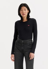 T-shirt noir à manches longues en tissu doux avec un col rond, arborant un petit logo rouge Levi's. Porté avec un jean taille haute gris foncé.