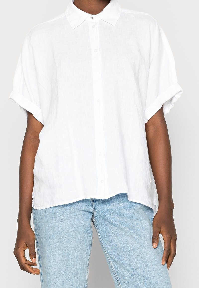 Vit linneskjorta med korta uppvikta ärmar, avslappnad passform och en subtil textur. I kombination med ljusblå denimjeans.
