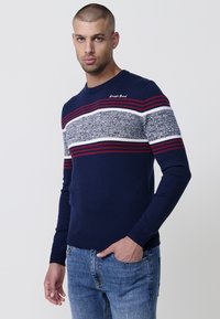 Suéter azul marino con cuello redondo, con rayas horizontales en rojo, blanco y un tejido texturizado gris. Puños y dobladillo de canalé.