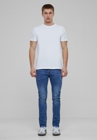 Camiseta blanca de manga corta, jeans ajustados azules con detalles de salpicaduras de pintura y zapatillas grises con acentos en blanco y negro.
