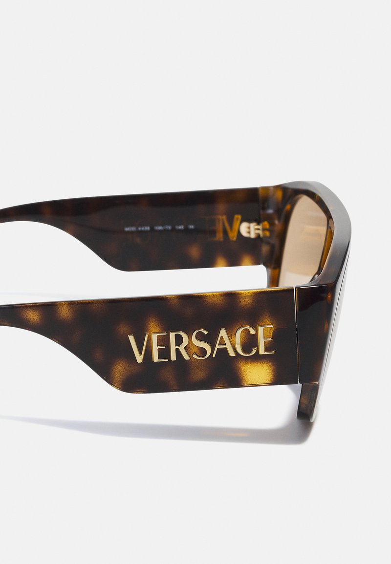 Schildpaddenbruine zonnebril met gouden "VERSACE" logo op de poot. Dikke montuur, licht oversized, met een gepolijste afwerking en gradient lenzen.