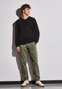 Svart v-ringad tröja, olivgröna byxor och beige sneakers. Tröjan har en slim fit, medan byxorna har sidfickor och en rak passform.