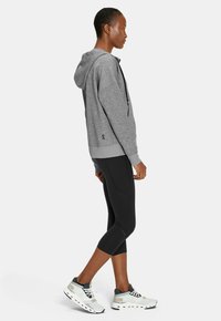 Grauer Kapuzenpullover mit lässiger Passform, kombiniert mit schwarzen Leggings und hellen Sneakers mit grauen und weißen Akzenten.