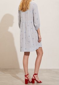 Jasnoniebieska sukienka z krótkim rękawem, ozdobiona haftem kwiatowym, o warstwowym kroju i rozszerzanym fasonie. Połączona z czerwonymi sandałami na wysokim obcasie.