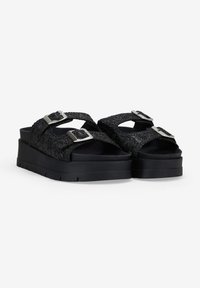 Black platform sandals with textured fabric straps and silver metal buckles, featuring a cushioned sole and a sturdy, flat base.