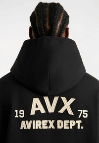 Felpa nera con cappuccio, caratterizzata da un grande testo ricamato sul retro: "AVX 1975 AVIREX DEPT." con fili di colore crema in contrasto.