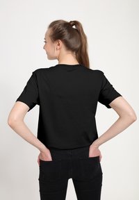 Černé bavlněné tričko s krátkým rukávem a kulatým výstřihem, zobrazené zezadu, s volným střihem a hladkou strukturou.