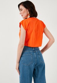 Orange cropped t-shirt med korte ærmer, parret med højtaljede blå denim jeans. Glat bomuldsstof. Minimalistisk design.