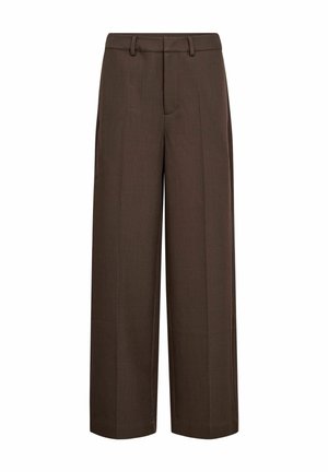 Gros plan d'une personne portant un pantalon marron foncé ajusté et un haut blanc côtelé, main reposant sur le côté.