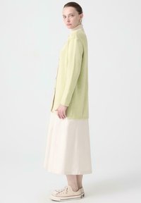 Lichtgroene geribbelde cardigan met knopen, gecombineerd met een crèmekleurige rok en beige sneakers. Eenvoudige, relaxte pasvorm en zachte textuur.