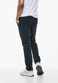 Chinos azul marino oscuro con un ajuste Slim, fabricados en algodón, con bolsillos laterales y traseros, combinados con zapatillas de color claro.