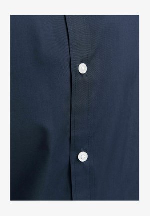 Gros plan sur le devant d'une chemise bleu marine montrant deux boutons blancs avec une couture soignée le long de la patte de boutonnage.