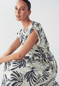 Oblačilo s cvetličnim vzorcem v kremni in mornarski barvi, z kratkimi nabranimi rokavi, elastičnim pasom in ohlapno krilo z vzorcem listov.