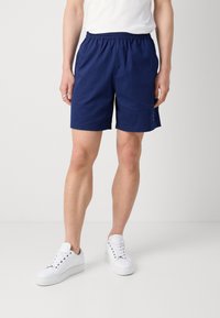 Mörkblå shorts i lätt tyg, med elastisk midja och sidofickor. Kombineras med vita sneakers.