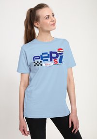 Světle modré bavlněné tričko s grafickým potiskem "PEPSI", šachovnicovým vzorem a ikonou globu. Krátké rukávy a volný střih.