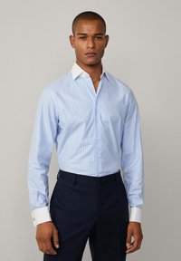 Lichtblauw gestreept overhemd met een witte kraag, met lange mouwen en een knoopsluiting aan de voorkant. Gecombineerd met donkerblauwe broek. Zachte stoftextuur.