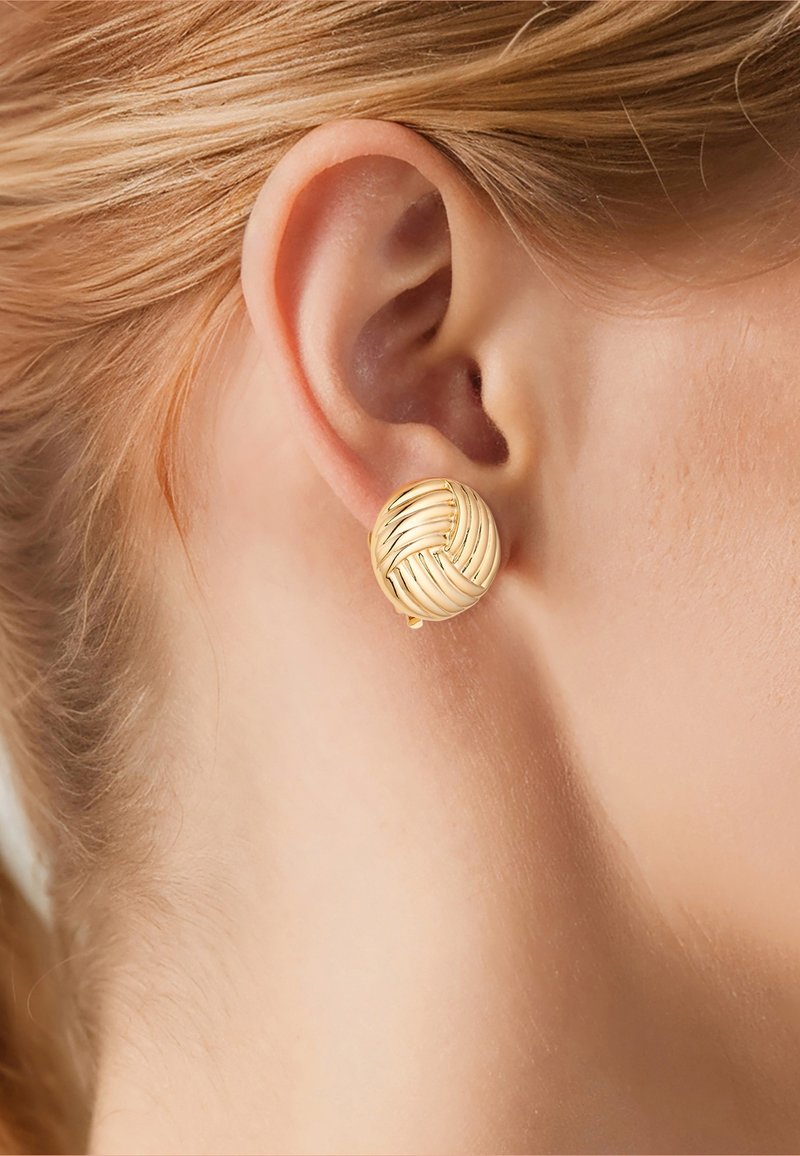 Close-up van het oor van een blond persoon met een ronde, gouden oorstekker met geweven patroon.