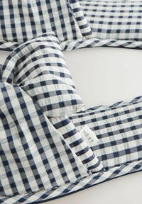 Mėlynos ir baltos spalvų languota minkšta medžiaga su nedideliu sulankstytu kampu ir matoma etiketė „NEXT“ ant šviesaus pagrindo.