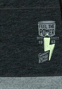 Tela de color gris oscuro con una sección inferior de color gris claro. Presenta el texto "SIENTE EL PODER" y un gráfico de un rayo en color verde claro.
