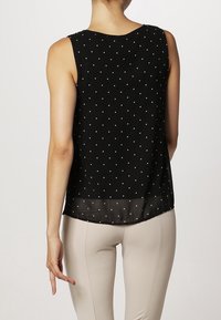 Top sin mangas negro con lunares blancos, dobladillo inferior transparente, cuello redondo y un corte relajado, que ofrece una sensación ligera.