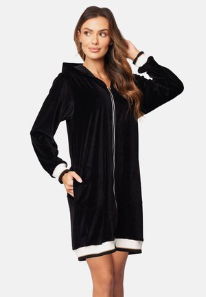 Black velour hoodie dress with zip closure, long sleeves, side pockets, and ribbed white cuffs and hem. Smooth texture and relaxed fit.