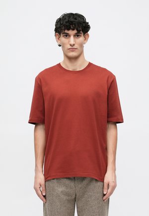 Camiseta de algodón roja con cuello redondo y mangas cortas, con un corte holgado y diseño minimalista. Combinada con pantalones de cuadros grises texturizados.