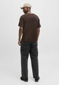 Brun kortærmet t-shirt med en afslappet pasform, parret med mørkegrå løse jeans. En beige cap fuldender looket. Minimalistisk design.
