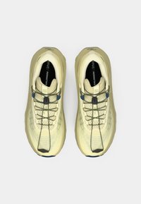 Μπεζ αθλητικά παπούτσια με υφή στο άνω μέρος, μαύρα πέλματα και γκρι κορδόνια. Διαθέτουν καλουπωμένη σόλα και μπλε λεπτομέρειες κοντά στα κορδόνια.