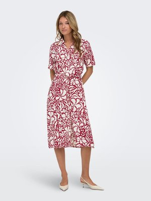 Kvinde iført en rød og hvid blomsterprintet midi-kjole med korte ærmer, krave, bælte og cremefarvede lavhælede slingback sko.