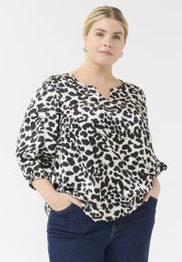 Blůza s leopardím potiskem v černobílé barvě, s výstřihem do V a nabíranými rukávy, vyrobená z lesklé tkaniny. V kombinaci s tmavě modrými džíny.