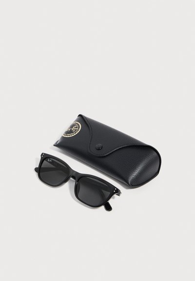 Черни слънчеви очила Ray-Ban с тъмни лещи, поставени до черен текстуриран кожен калъф с златен лого надпис на бял фон.