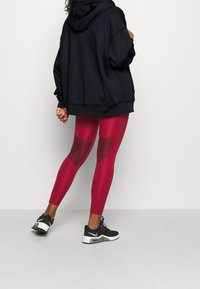 Leggings rojos con detalles de malla, combinados con una sudadera negra holgada y zapatillas deportivas negras. Tejido suave y diseño ajustado.