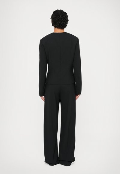 Costum negru personalizat, cu un sacou ajustat, guler înalt și mâneci lungi, asortat cu pantaloni evazați. Textură netedă, design minimalist.