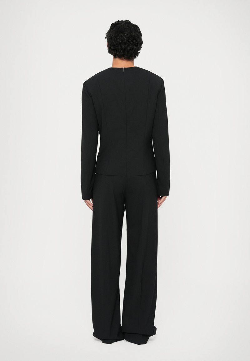 Tailored black suit featuring a fitted jacket with a high neckline and long sleeves, paired with wide-leg trousers. Smooth texture, minimal design.