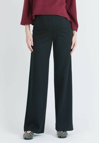 Black wide-leg trousers made of a smooth fabric, paired with a maroon top. Footwear features a pattern of white dots on a black background.