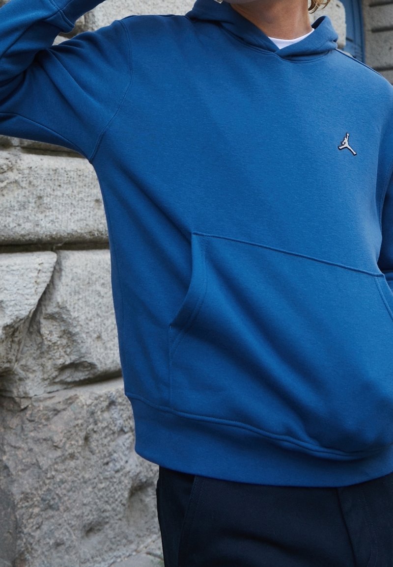 Hoodie in cotone blu con tasca frontale, cappuccio con lacci e un piccolo logo sul petto. Presenta una texture liscia e una vestibilità comoda.