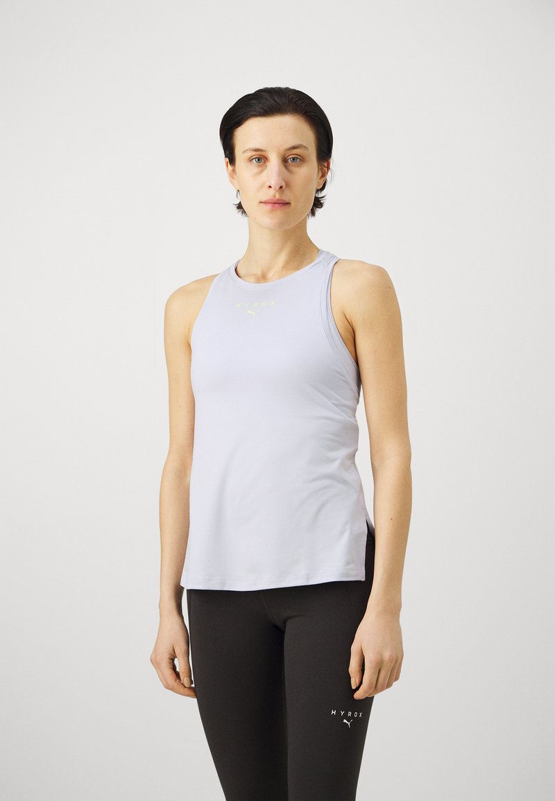 Helles graues Sporttanktop mit rundem Ausschnitt und ärmellosem Design, das ein subtile Logo in Neon-Grün aufweist. Kombiniert mit schwarzen Leggings.