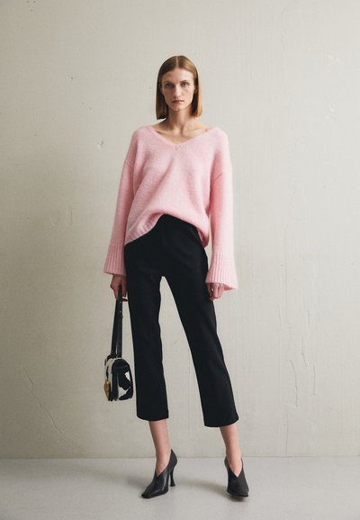 Pink oversized sweater with a V-neck, textured fabric, black cropped pants, and black high-heeled shoes, paired with a small bag.