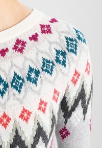 Stickad tröja i ljusgrått med flerfärgade geometriska mönster, inklusive rosa, teal och röda accenter, med en texturerad yta.