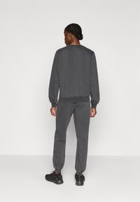 Siva trenerka in usklajevanje hlač iz mehkega, teksturiranega blaga. Obleka ima rebraste manšete in sproščen kroj. Črne superge dopolnjujejo videz.