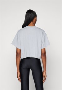 Vaaleanharmaa lyhythihainen croptop, jossa on pyöreä kaula-aukko ja sileä pinta, yhdistettynä mustiin korkeavyötäröisiin legginsseihin.