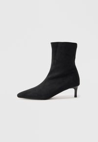 Stivale alla caviglia in suede nero con punta appuntita e tacco sottile e leggermente curvato. Texture liscia e design minimalista.